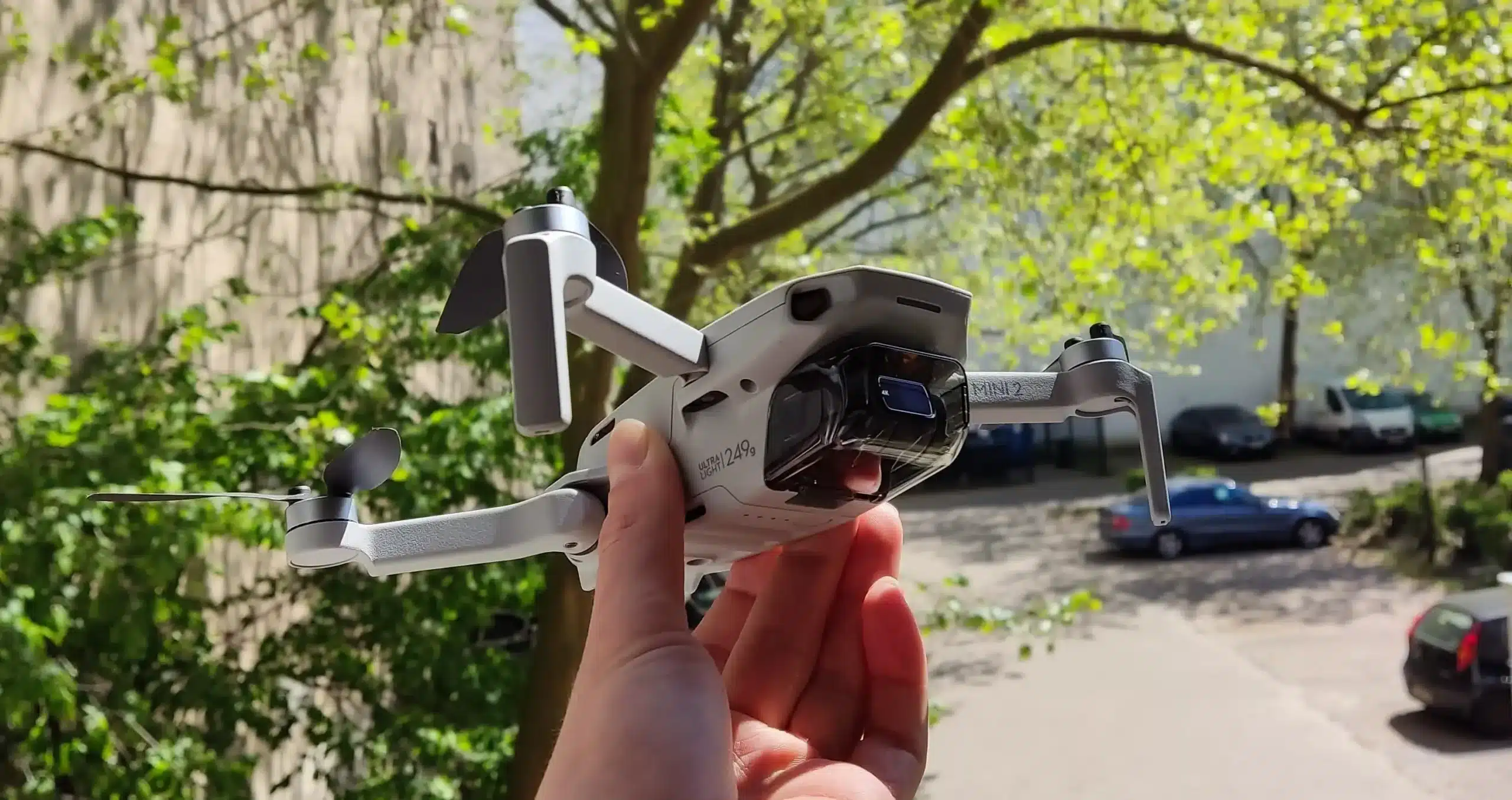 Drohne DJI Mini 2 nach oben gerichtet wird in der Hand gehalten im Hintergrund Bäume und ein Parkplatz